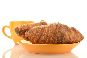 Two appetizing croissants with chocolate filling on a saucer with a cup close-up, isolated on white.