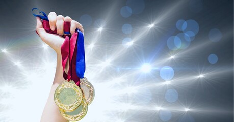 Close up of hand holding multiple medals against shining star lights and spots of light