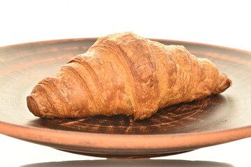 One fragrant croissant with chocolate filling on a plate of clay, close-up, isolated on white.