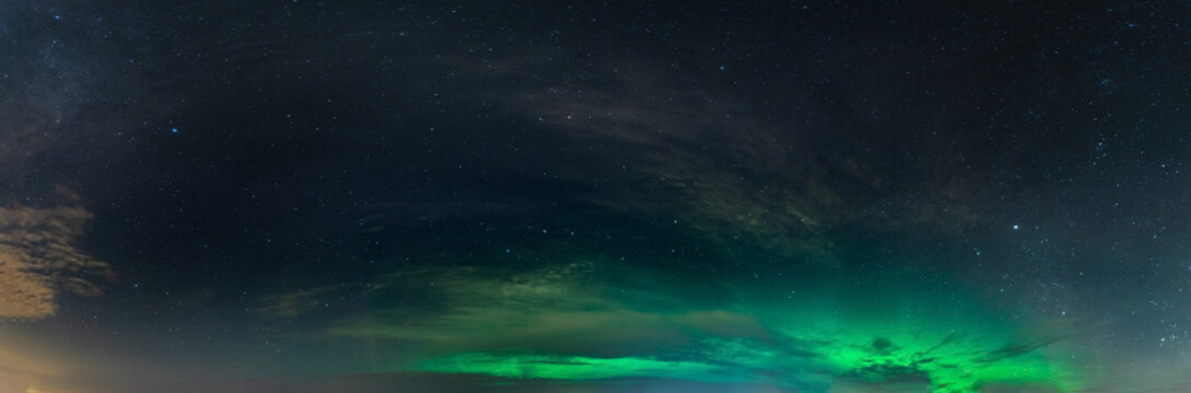 Panoramic real photo of beautiful soft Aurora Borealis - bright green lights on black night sky with some clouds. A lot of real stars seen in Northern hemisphere, background picture