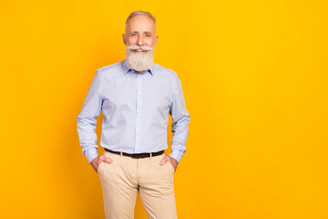 Photo of cheerful beard elder man stand wear blue shirt pants isolated on yellow color background