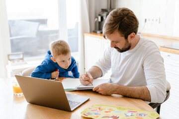 Fototapeta na wymiar White father and son drawing and using laptop in kitchen at home
