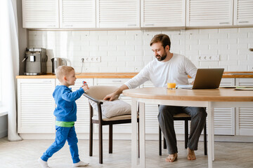 White father playing with his son and using laptop in kitchen