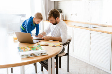Obraz premium White father and son drawing and using laptop in kitchen at home
