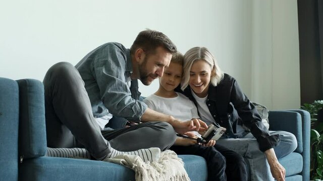 Happy family adult parents with cute school kids children relax on sofa using funny smartphone apps laughing having fun with technology together looking at phone screen take selfie play game at home