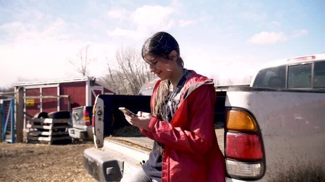 Teenage girl using smart phone at truck bed on sunny farm