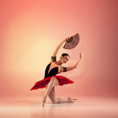 Young and incredibly beautiful ballerina is posing and dancing at red studio full of light.
