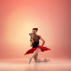 Young and incredibly beautiful ballerina is posing and dancing at red studio full of light.