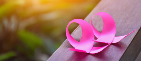 Pink ribbons on wooden table, sunlight and blurred background, concept for breast cancer awareness around the world. Soft and selective focus on pink ribbons.