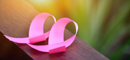 Pink ribbons on wooden table, sunlight and blurred background, concept for breast cancer awareness...