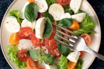 close up mozzarella, tomatoes basil leaf on a fork on a background of vegetable salad with cheese. Top view.