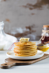 The pancakes are stacked in a plate with a piece of butter and drizzled with honey sauce. Breakfast concept.