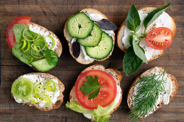 various vegetable sandwiches with cream cheese, tomatoes, dill, cucumbers, leeks and basil. serving a vegetarian sandwiches for appetizers on cutting board. top view
