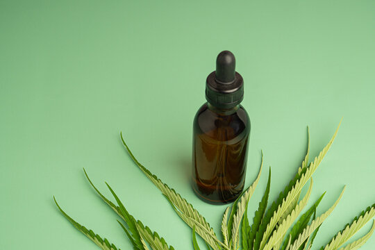 Medicinal cannabis with extract oil in a bottle and marijuana leaves on a green background.