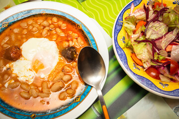 Closeup of a traditional Spanish Fabada asturiana with poached egg and mixed salad. white beans recipe