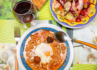 Closeup of a traditional Spanish Fabada asturiana with poached egg and mixed salad. white beans recipe
