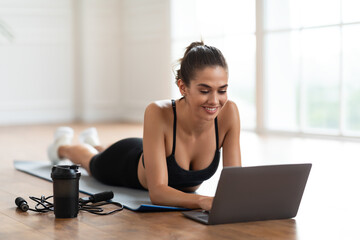 Obraz premium Young woman lying on yoga mat using laptop