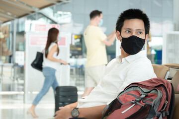 Fototapeta na wymiar Asian traveler man wearing face mask waiting to board into airplane, standing in departure terminal in airport. Male passenger traveling by plane transportation during covid19 virus pandemic