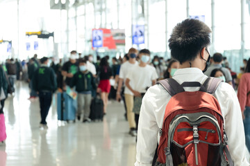 Asian traveler man wearing face mask waiting to board into airplane, standing in departure terminal in airport. Male passenger traveling by plane transportation during covid19 virus pandemic