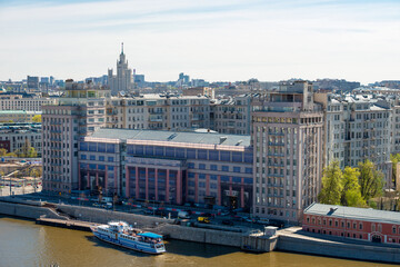 Obraz premium Top view of a house on the embankment on Berezhkovskaya embankment with the Estrada theater and a pleasure boat at the pier of the Moskva River on a spring day