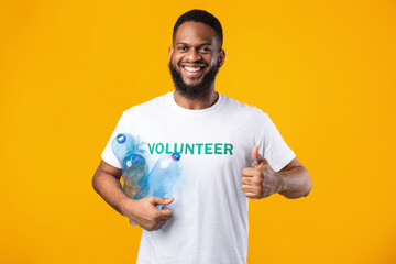 Black Volunteer Man Holding Plastic Bottles Gesturing Thumbs-Up, Yellow Background