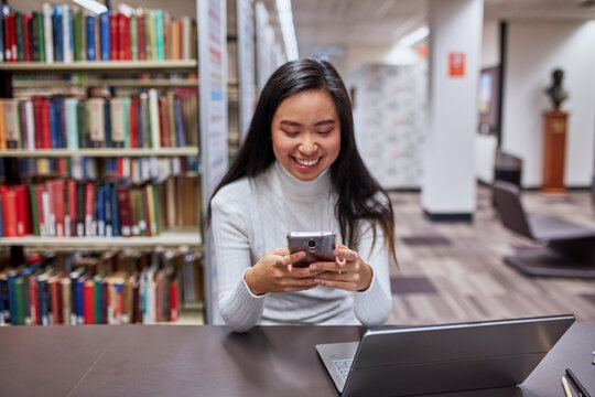 Young Asian student on phone at university library