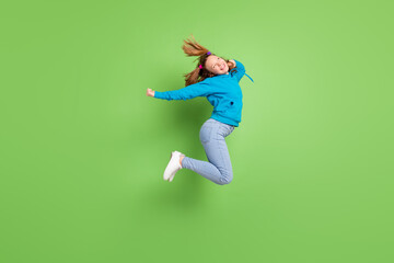 Full body photo of dreamy happy young girl jump up look empty space fly hair isolated on green color background
