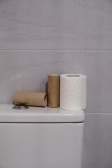 White toilet with some finished rolls of paper and others without touching.