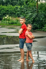 Fototapeta na wymiar Happy children in a puddle. Brother and sister are walking barefoot after a summer rain.