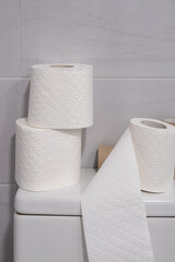 White toilet with some finished rolls of paper and others without touching.