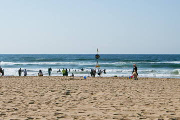 A beach filled with beach goers around a designated swimming area sign on a sunny day in Durban, South Africa