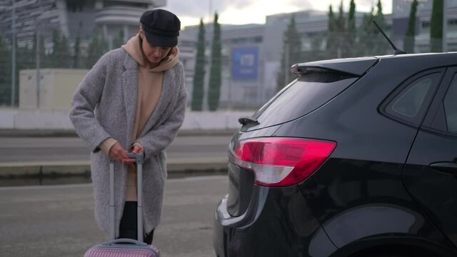 young woman is opening trunk of her auto and putting suitcase inside