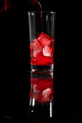 Pouring red juice on the top of the ice into the glass against complete dark background. copy space. Pour alcohol,
