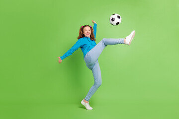 Full length photo of happy nice young little girl play soccer good mood kick isolated on green color background - obrazy, fototapety, plakaty