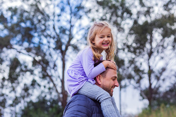 Happy little girl riding on her dads shoulders on cold overcast autumn day