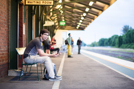Uni student sitting on bench at train station waiting for train