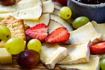 cheese assorted with fruit on wooden board.