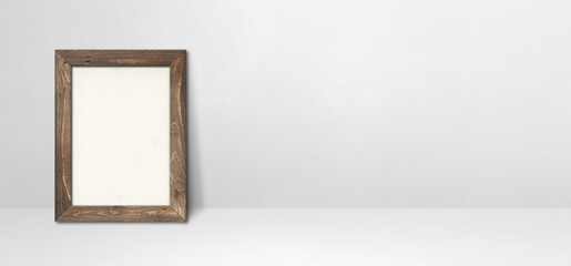 Wooden picture frame leaning on a white wall. Horizontal banner