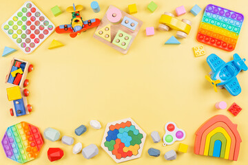 Baby kids toys background with educational wooden toys, train, plane, pop it fidget toys on yellow background. Top view, flat lay, copy space for text