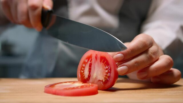 Female hands cut red tomato in slices