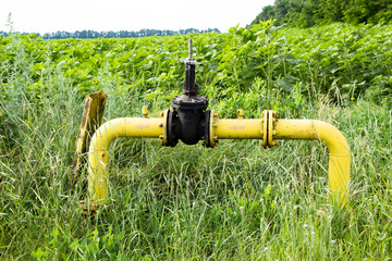Yellow gas pipe with black valve in the field near the field with sunflower Ukraine