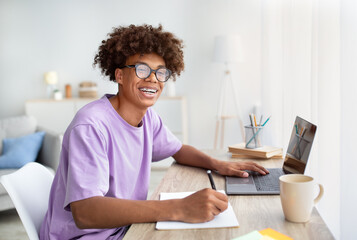 E-learning concept. Portrait of smiling African American teenager having web lesson on laptop,...