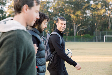 Close up photo of 3 young interracial men walking on the soccer field