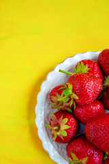 Ripe red sweet strawberry on a white plate on a yellow background