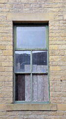 boarded up window with broken panes in an old abandoned house with stone walls and green frame