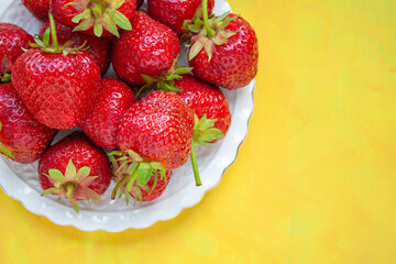 Sweet strawberry on a white plate on a yellow textured background