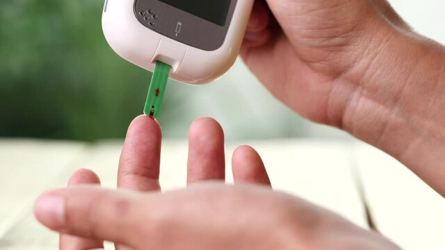 Close up diabetic test using lancet pen ad glucometer on finger with blood drop checking sugar level. Concept of World Diabetes Day, Glycemia, Hyperglycemia, Insulin, Healthcare and Medical.