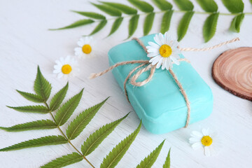 Green soap with chamomile on a light background next to green leaves. The concept of the natural use of funds. Spa and sauna