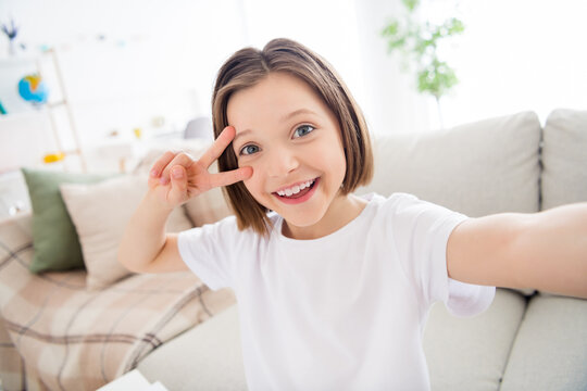 Photo of young attractive small kid girl happy positive smile show peace cool v-sign make selfie home