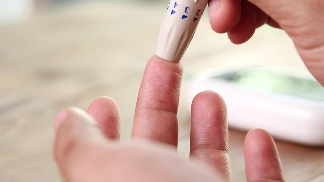 Close up diabetic test using lancet pen ad glucometer on finger with blood drop checking sugar level. Concept of World Diabetes Day, Glycemia, Hyperglycemia, Insulin, Healthcare and Medical.